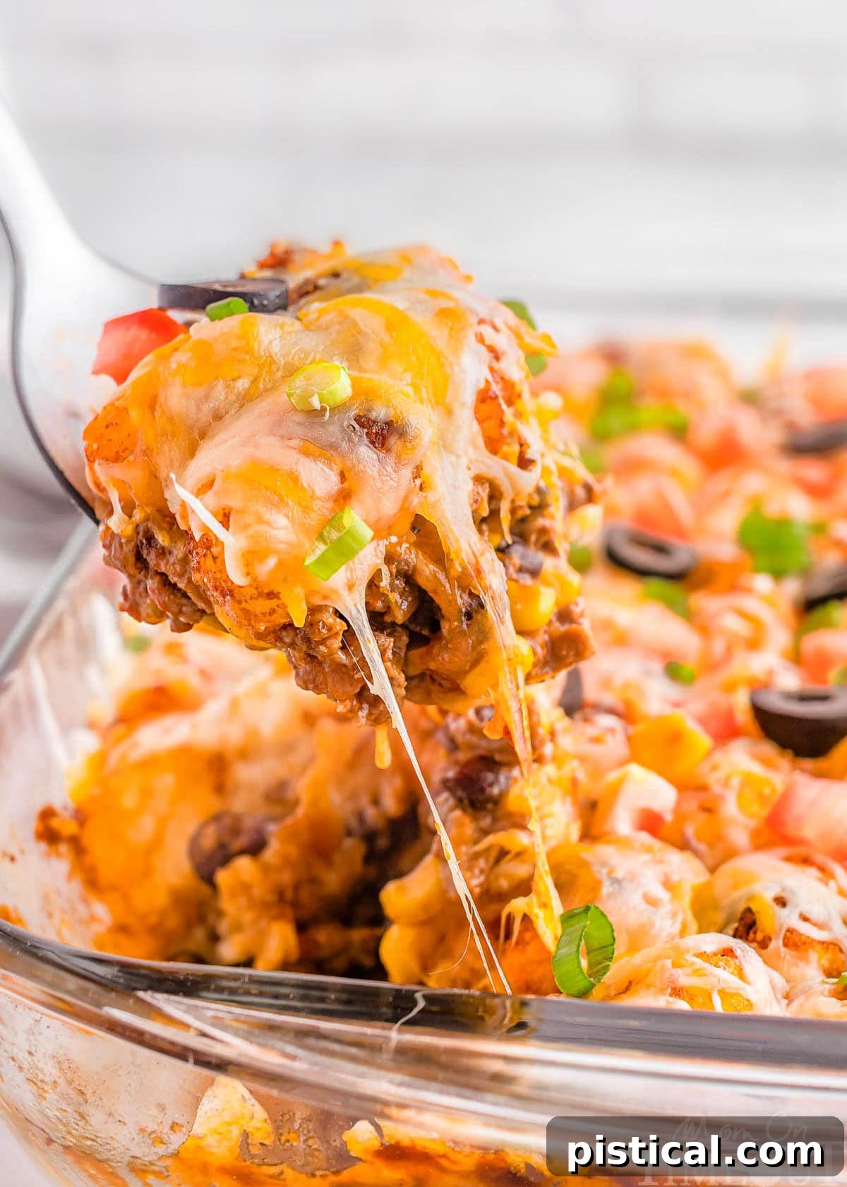 A spatula carefully scooping a perfect portion of Mexican Tater Tot Casserole out of a glass baking pan, showing its delectable layers and crispy top.