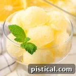 A beautiful glass bowl overflowing with scoops of vibrant homemade lemon sorbet, elegantly garnished with a fresh mint leaf.