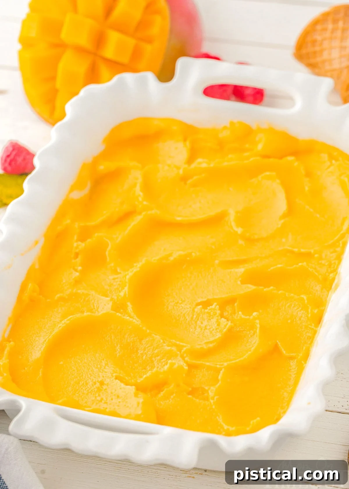A top-down view of vibrant mango sorbet spread evenly in a white pan, showcasing its smooth texture.