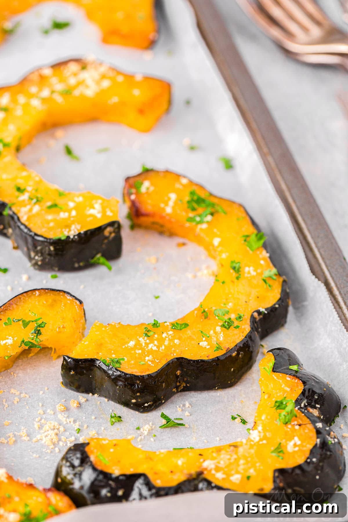 Roasted acorn squash slices arranged neatly on a sheet pan lined with parchment paper, highlighting their golden-brown edges.