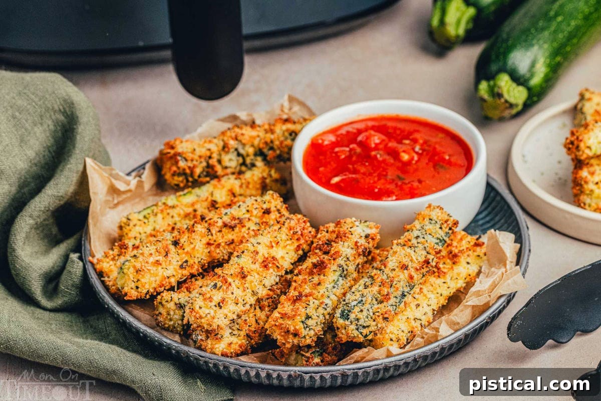 Wide shot of zucchini fries on a metal plate with black air fryer in the background, highlighting the ease of making this delicious snack or side dish.