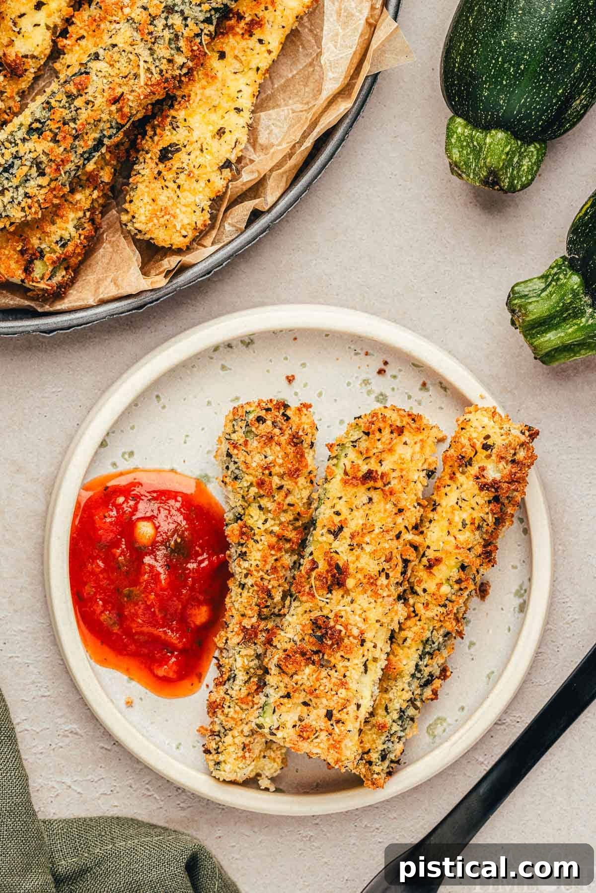 Top down view of small round white plate with three zucchini fries on it and a dollop of marinara, perfectly portioned for a delightful snack or appetizer.
