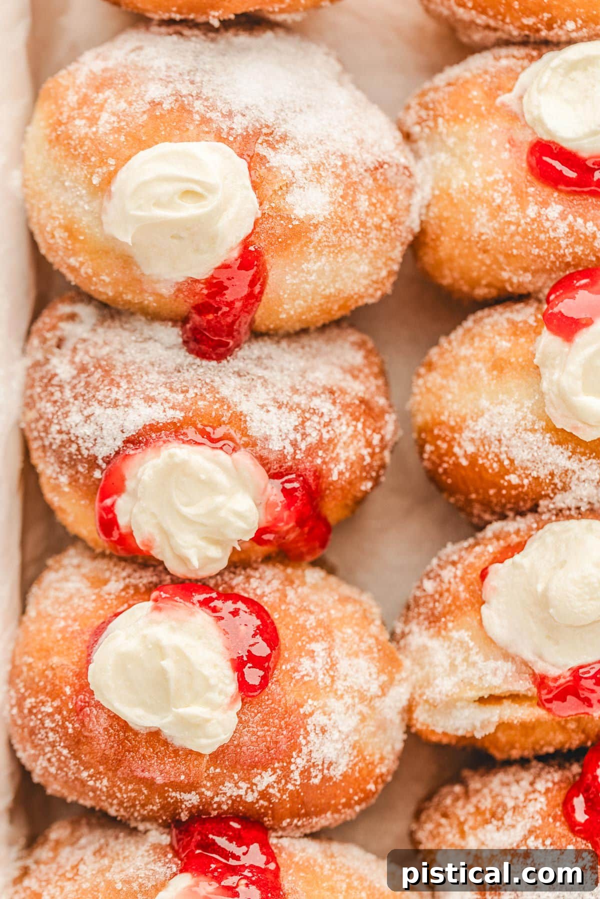 Top-down shot of a box filled with beautifully arranged raspberry cheesecake stuffed donuts, glistening with a sugar coating.