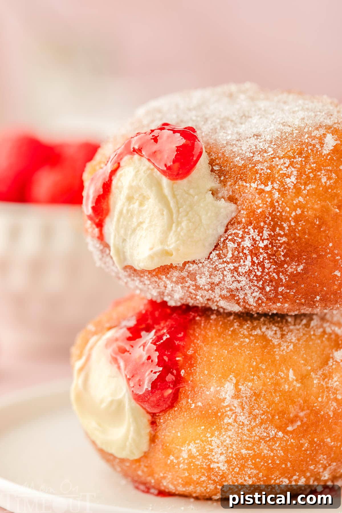 Two homemade donuts generously stuffed with cheesecake and raspberry compote, presented beautifully.