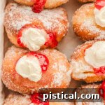 Top-down shot of stuffed raspberry cheesecake donuts lined up in a box, freshly rolled in sugar.