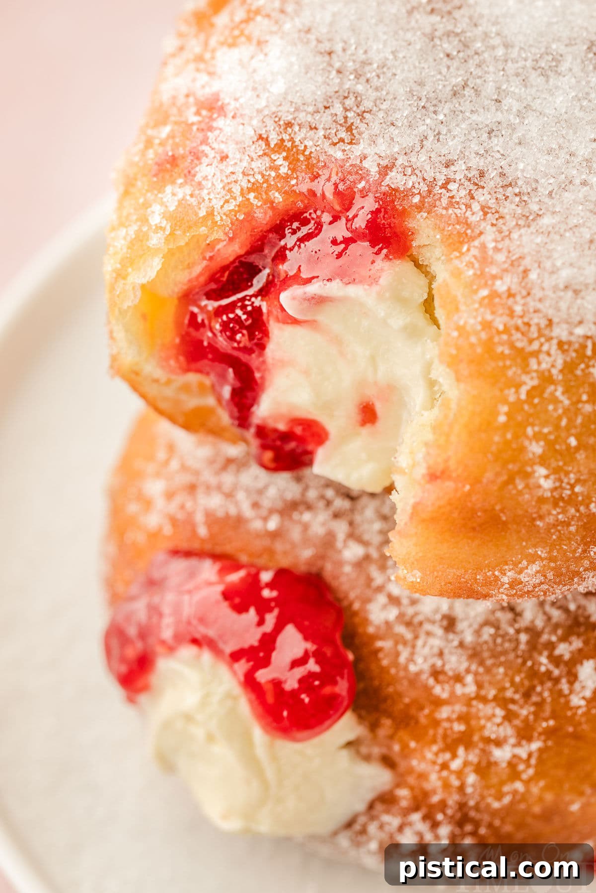 Top-down angled view of two raspberry cheesecake donuts stacked on each other, both with a bite taken out, highlighting the delicious layers.