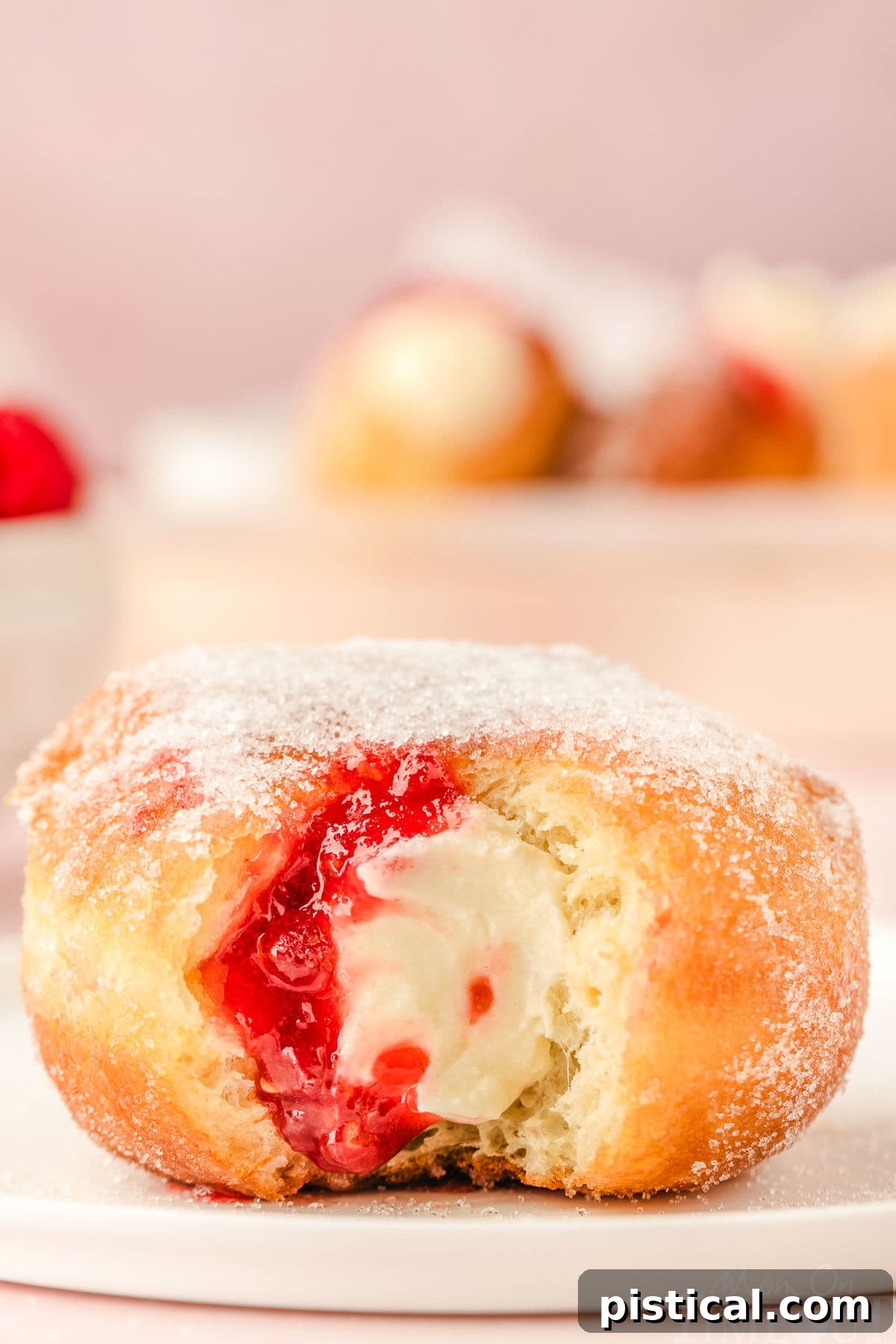 A single raspberry cheesecake stuffed donut on a small round white plate, with a portion bitten off, revealing its layers of filling.