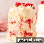 Slice of white chocolate raspberry cake on a white round plate topped with fresh raspberries and white chocolate curls.
