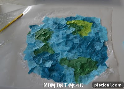Children placing torn tissue paper onto glue-covered wax paper to form an Earth design