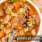 Hearty Beef Barley Stew 8 A top down view of a spoon in a bowl of beef and barley soup.
