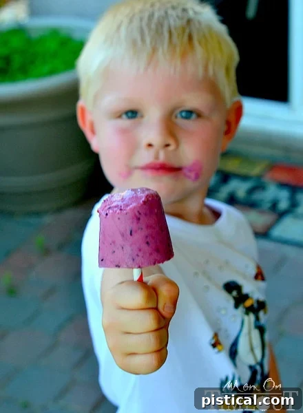 A young boy, Bryce, enjoying a Greek Yogurt Berry Smoothie Pop, showcasing its appeal to children.