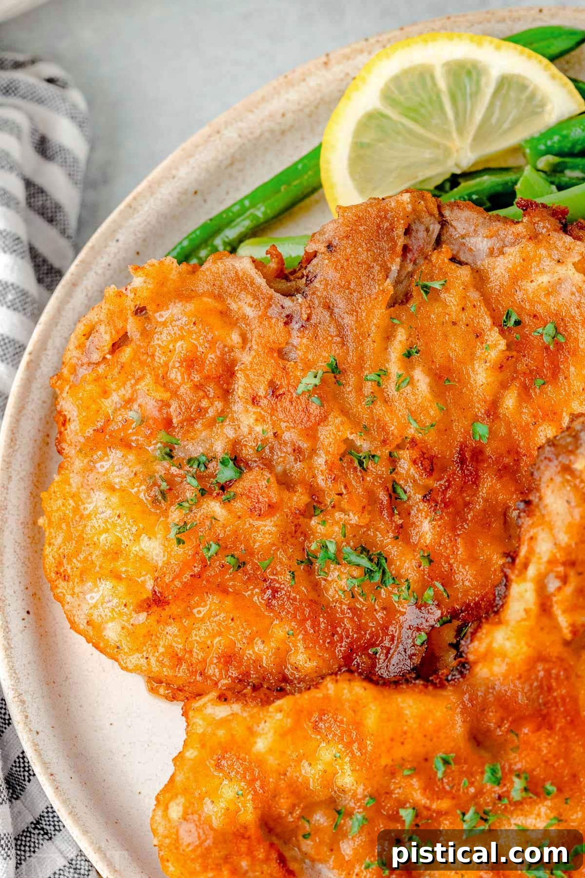 A close-up view of perfectly fried pork chops served on a pristine white plate, highlighting their golden, crispy breading and inviting texture. The detail shows the seasoning clinging beautifully to the crust.