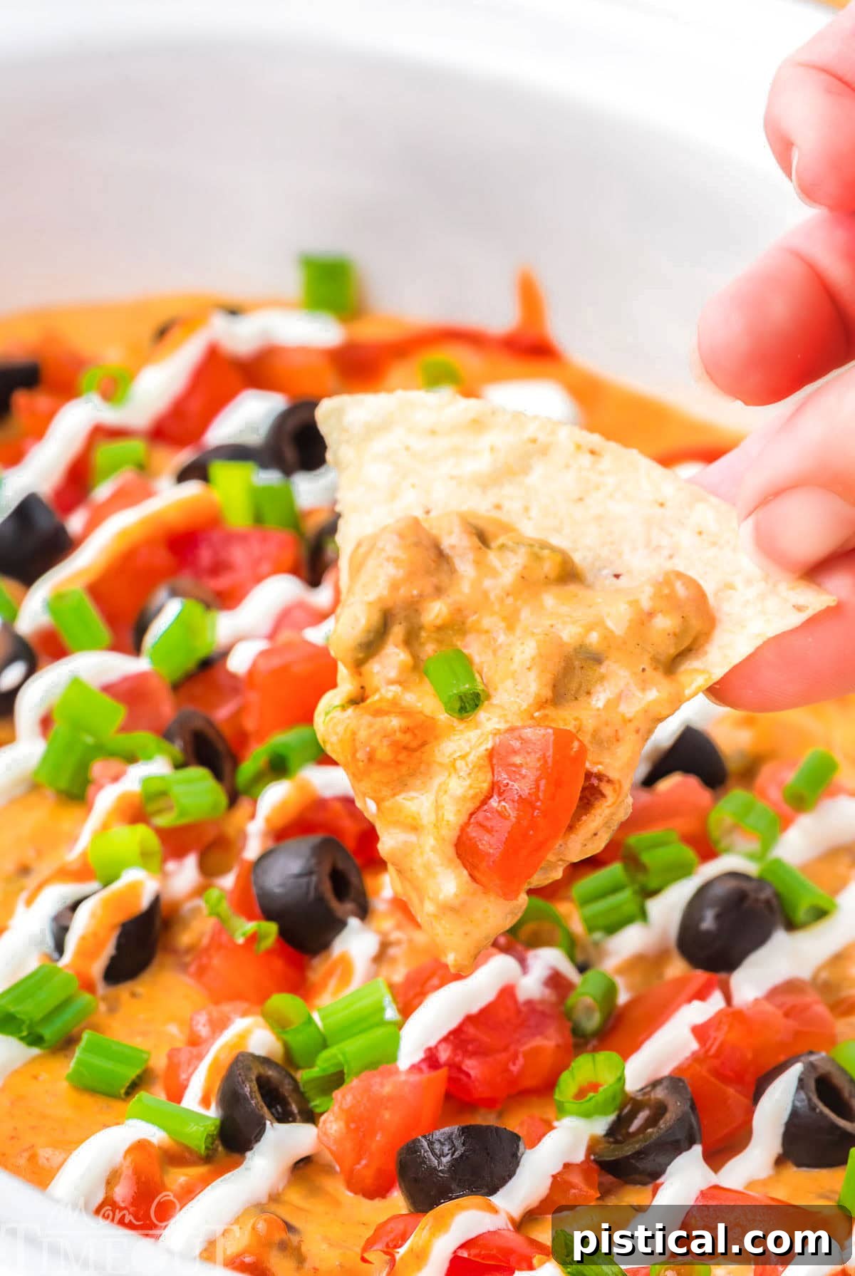 Warm & Cheesy Slow Cooker Taco Dip 7 A hand holding up a tortilla chip with crockpot taco dip on it.