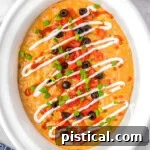 Warm & Cheesy Slow Cooker Taco Dip 9 Top down view of crockpot taco dip in a white crockpot. The dip has been topped with lots of taco toppings.