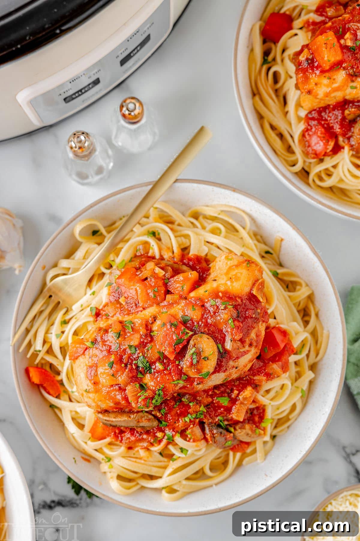 Slow Cooker Chicken Cacciatore on a bed of pasta on a white plate next to a white slow cooker.