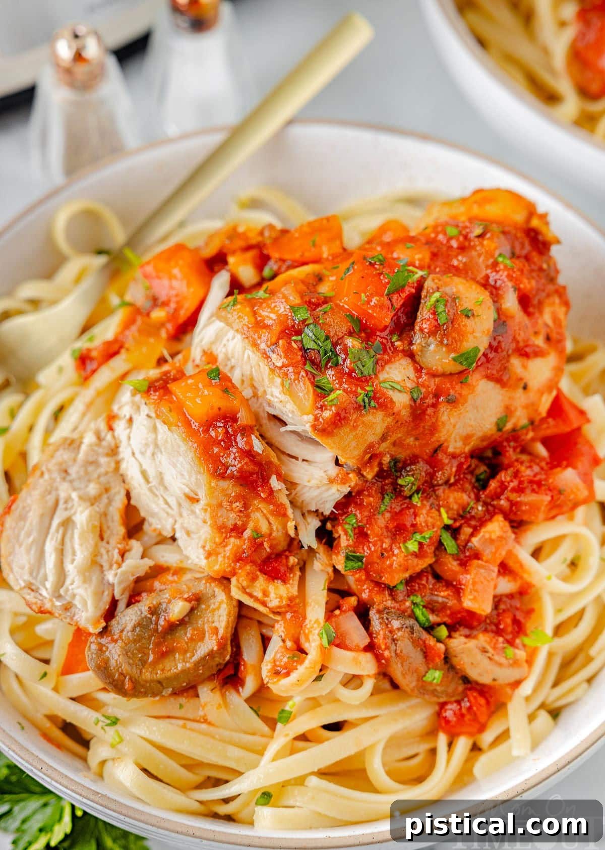A top down shot of chicken cacciatore sliced into pieces on a bed of pasta on a white plate.