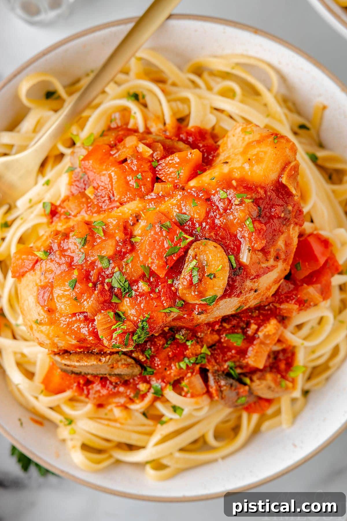 A top down shot of chicken cacciatore on a bed of pasta on a white plate.