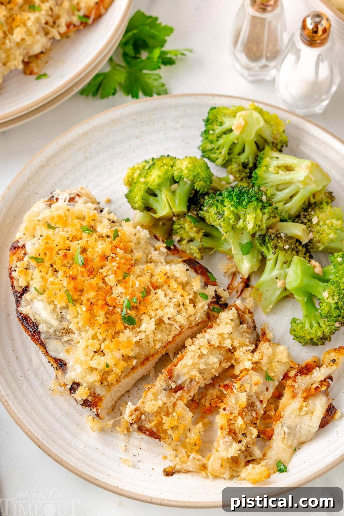 Steakhouse-Style Parmesan Crusted Chicken 8 Top down view of Longhorn Parmesan Crusted Chicken plated with roasted broccoli on a round white plate. The crispy Parmesan and Panko topping is clearly shown and a few strips of chicken have been cut off the breast.