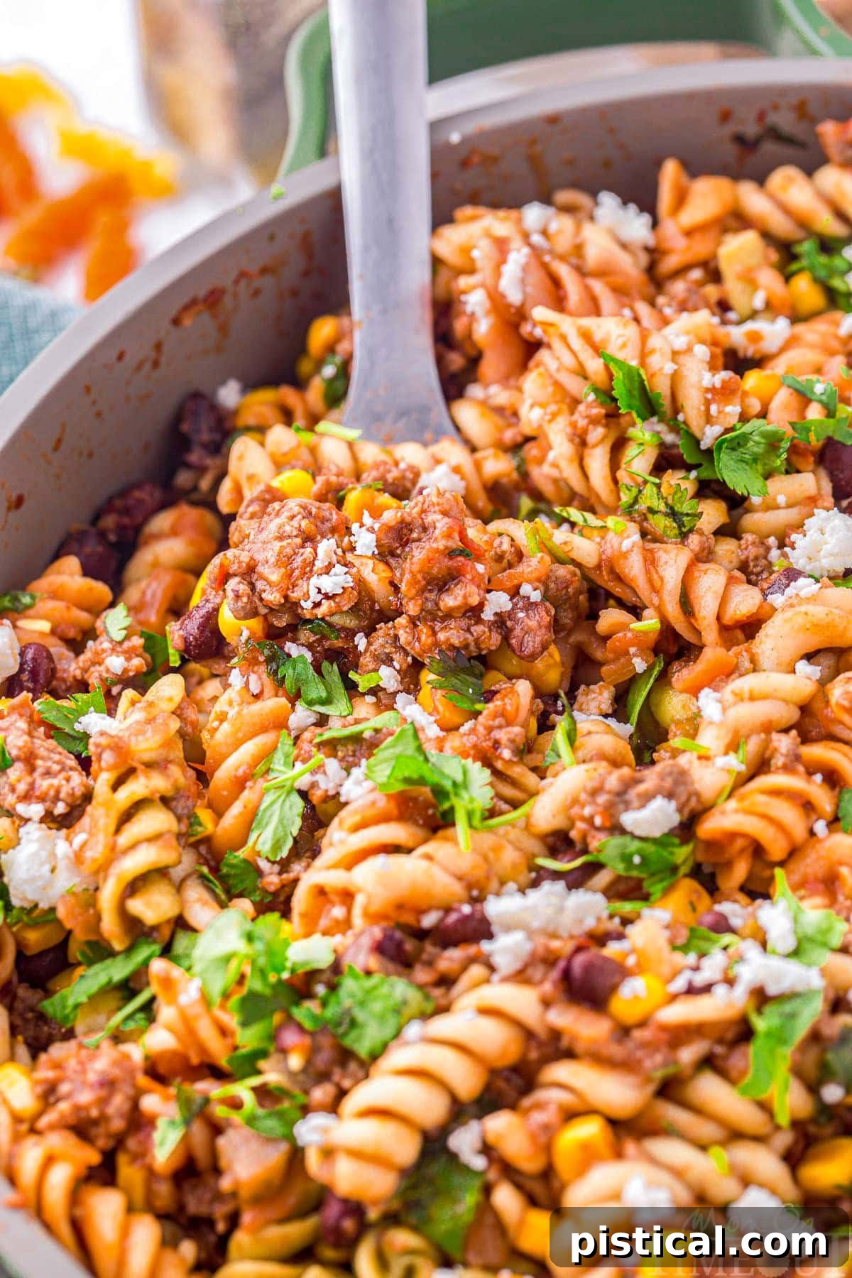Tex-Mex Pasta Skillet 5 A close-up view of vibrant taco pasta being scooped generously from a green skillet, showcasing the rich sauce and perfectly cooked ingredients. The steam rises gently, emphasizing its warmth and freshness.