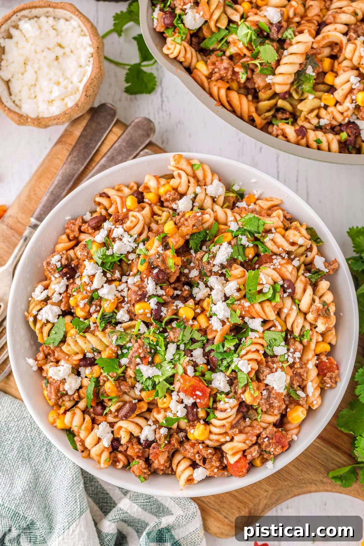 Tex-Mex Pasta Skillet 6 Top-down view of a round white bowl filled with freshly cooked taco pasta, positioned enticingly next to a green skillet holding the remaining portion of the delicious dish. The presentation highlights the meal's hearty and appealing nature.