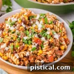 Tex-Mex Pasta Skillet 7 angled view of bowl filled with taco pasta and green skillet in the background with the rest of the taco pasta recipe.
