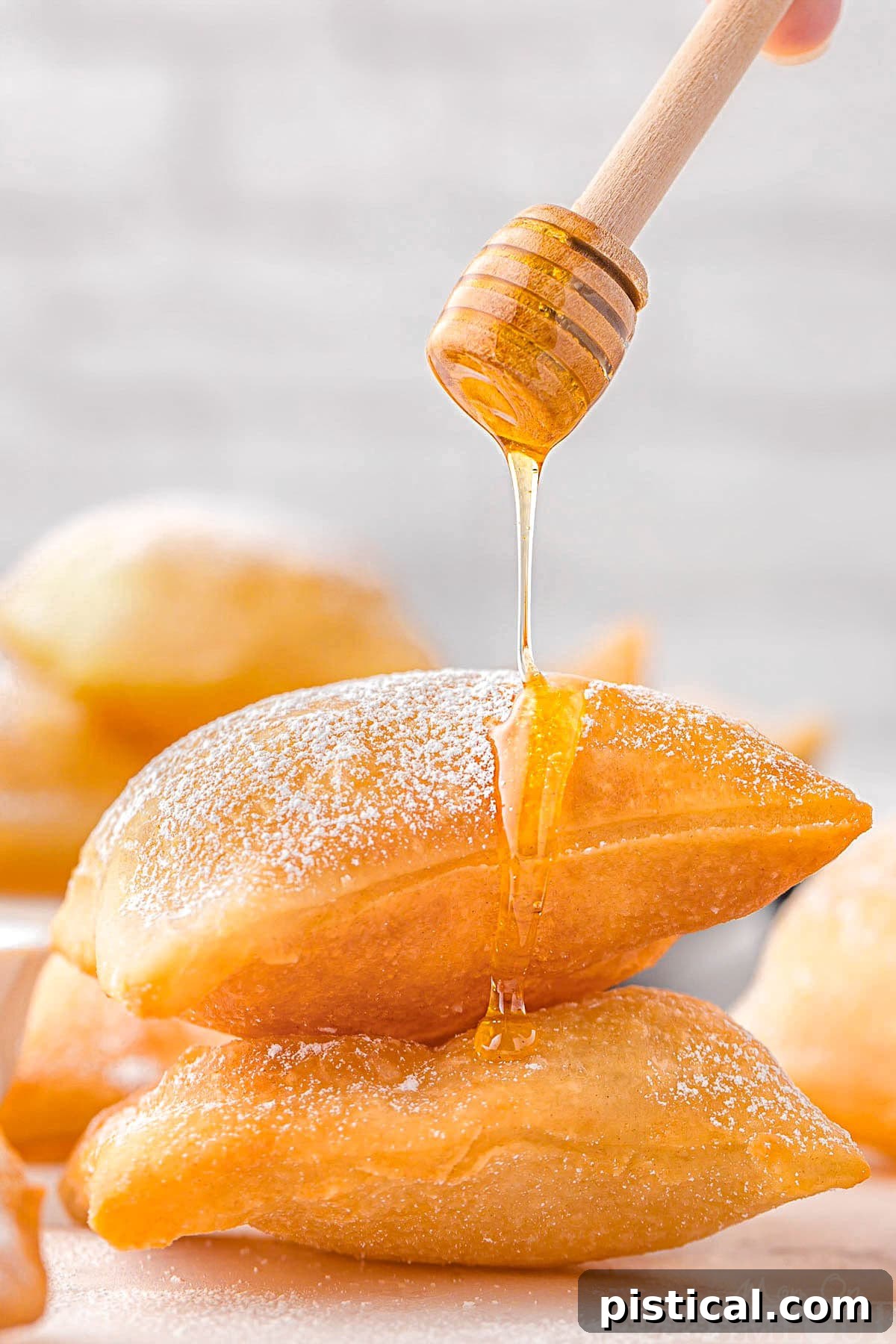 A stack of sopapillas with a honey dipper drizzling honey on top.