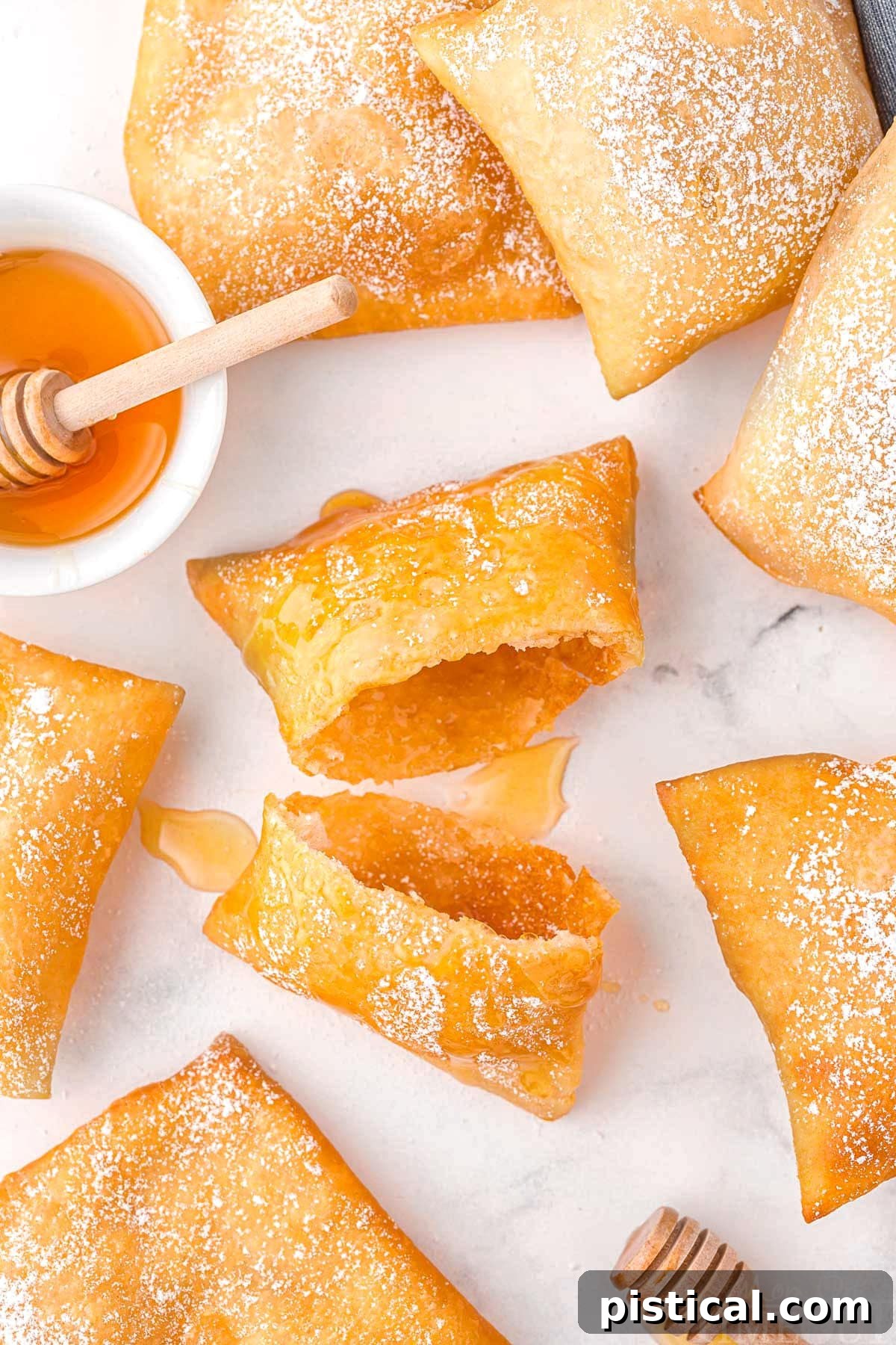 A sopapilla torn in half with additional sopapillas around it on a white surface.