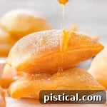 A stack of sopapillas with a honey dipper drizzling honey on top.