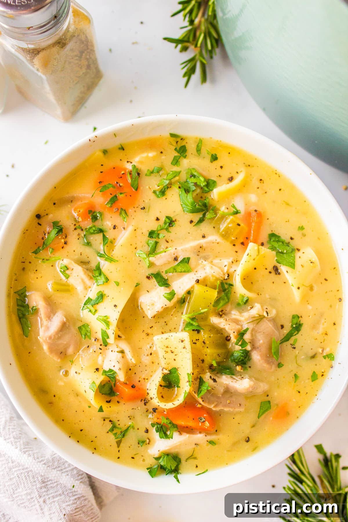 Silky Chicken Noodle Bliss 2 A top down shot of a white bowl of creamy chicken noodle soup garnished with fresh parsley.
