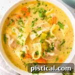A top down shot of a white bowl of creamy chicken noodle soup garnished with fresh parsley.
