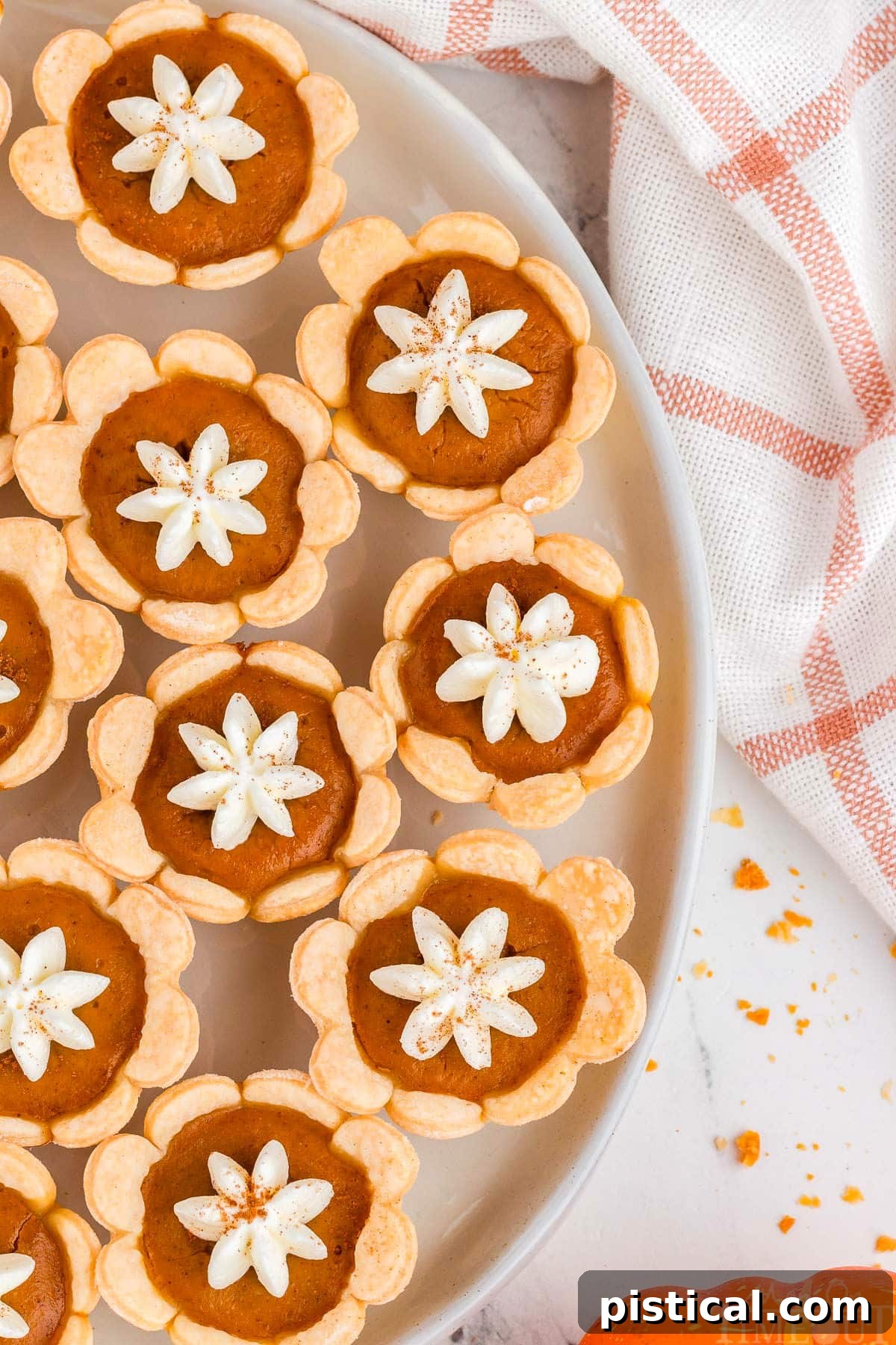 Top down shot of mini pumpkin pies with whipped cream dollops on a plate, alongside an elegant orange and white linen napkin.