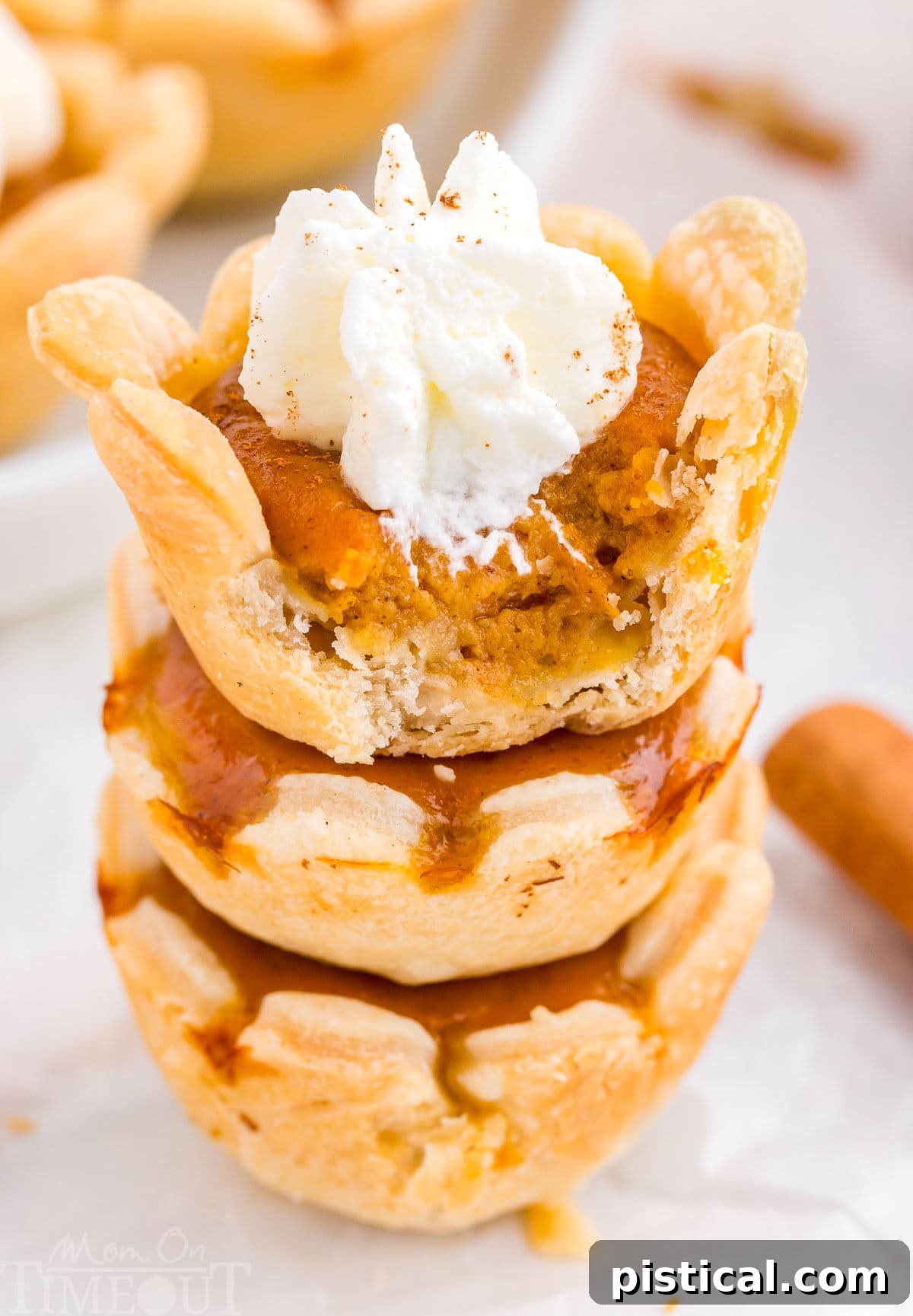 A stack of golden-brown mini pumpkin pies, with the top pie having a tempting bite taken out, revealing the creamy filling.