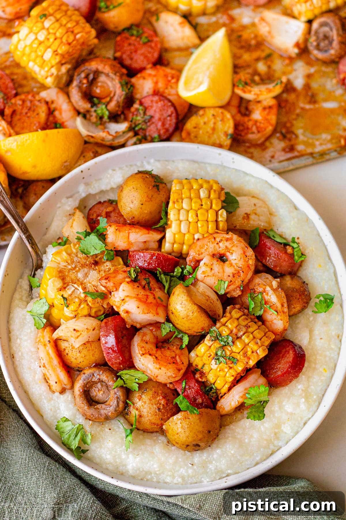 Shrimp boil in a bowl served with grits. The bowl is sitting next to a sheet pan with the rest of the shrimp boil.