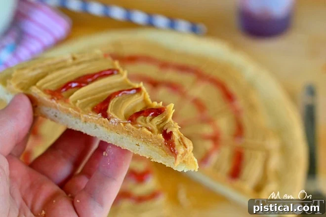 Peanut Butter and Jelly Sugar Cookie Pizza - Inspired by #Disney! from MomOnTimeout.com A delicious slice of Peanut Butter and Jelly Sugar Cookie Pizza, showcasing its appealing presentation and ready to be enjoyed.