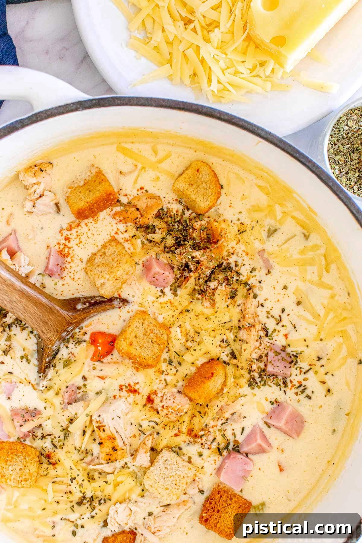A Bowl of Cordon Bleu Comfort 3 A top down shot of creamy chicken cordon bleu soup simmering in a Dutch oven, with a wooden spoon resting inside.