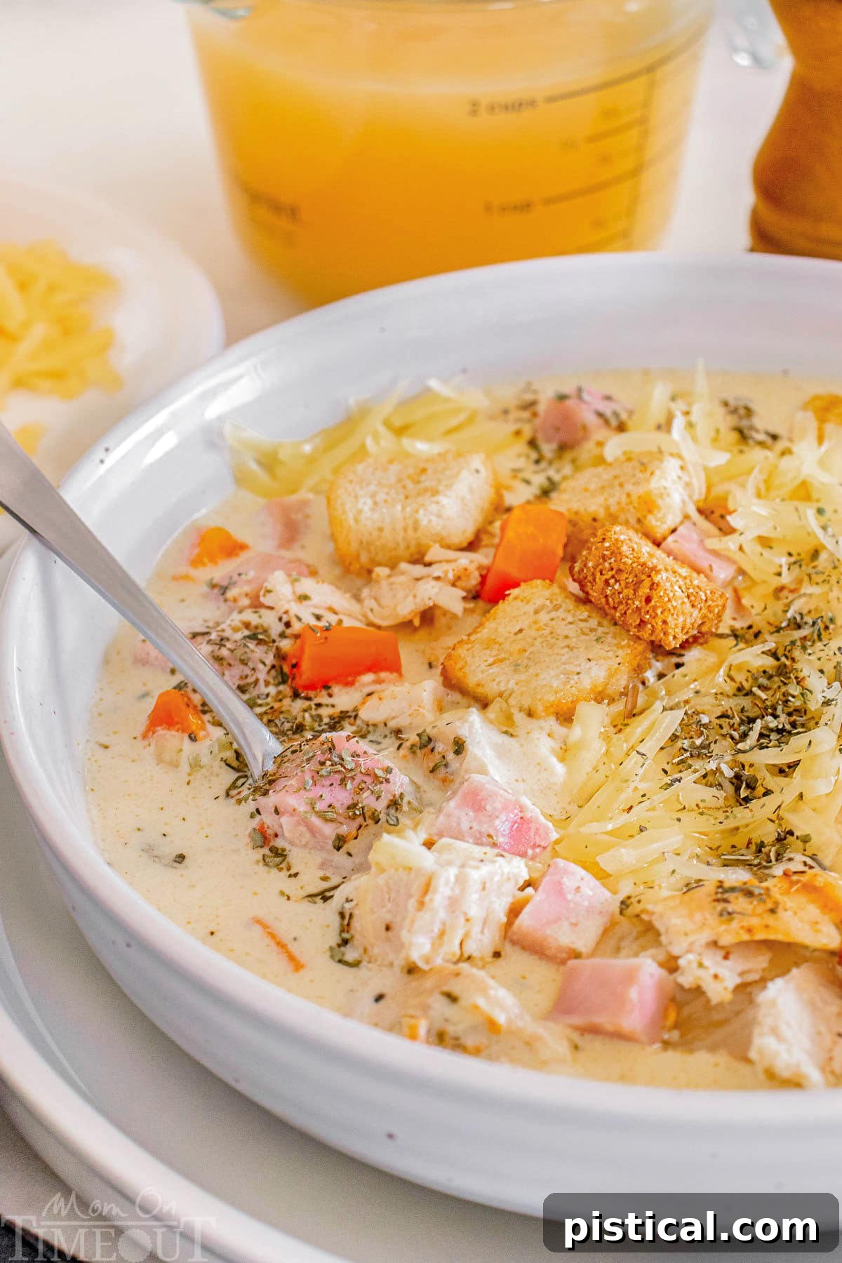 A Bowl of Cordon Bleu Comfort 6 A close-up photo of creamy chicken cordon bleu soup in a white bowl with a spoon resting in it, showcasing its rich texture and steam.