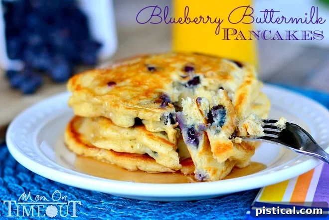 A stack of golden brown Blueberry Buttermilk Pancakes topped with maple syrup on a blue placemat.