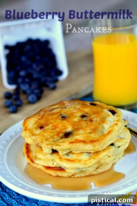 Close-up of a stack of Blueberry Buttermilk Pancakes with syrup and fresh blueberries in the background.