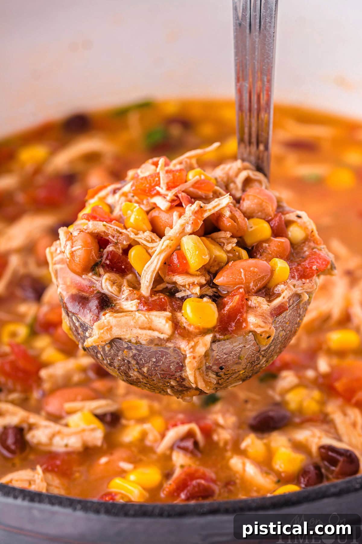 A soup ladle holding a scoop of flavorful chicken taco soup directly over the steaming pot of soup, ready to serve.