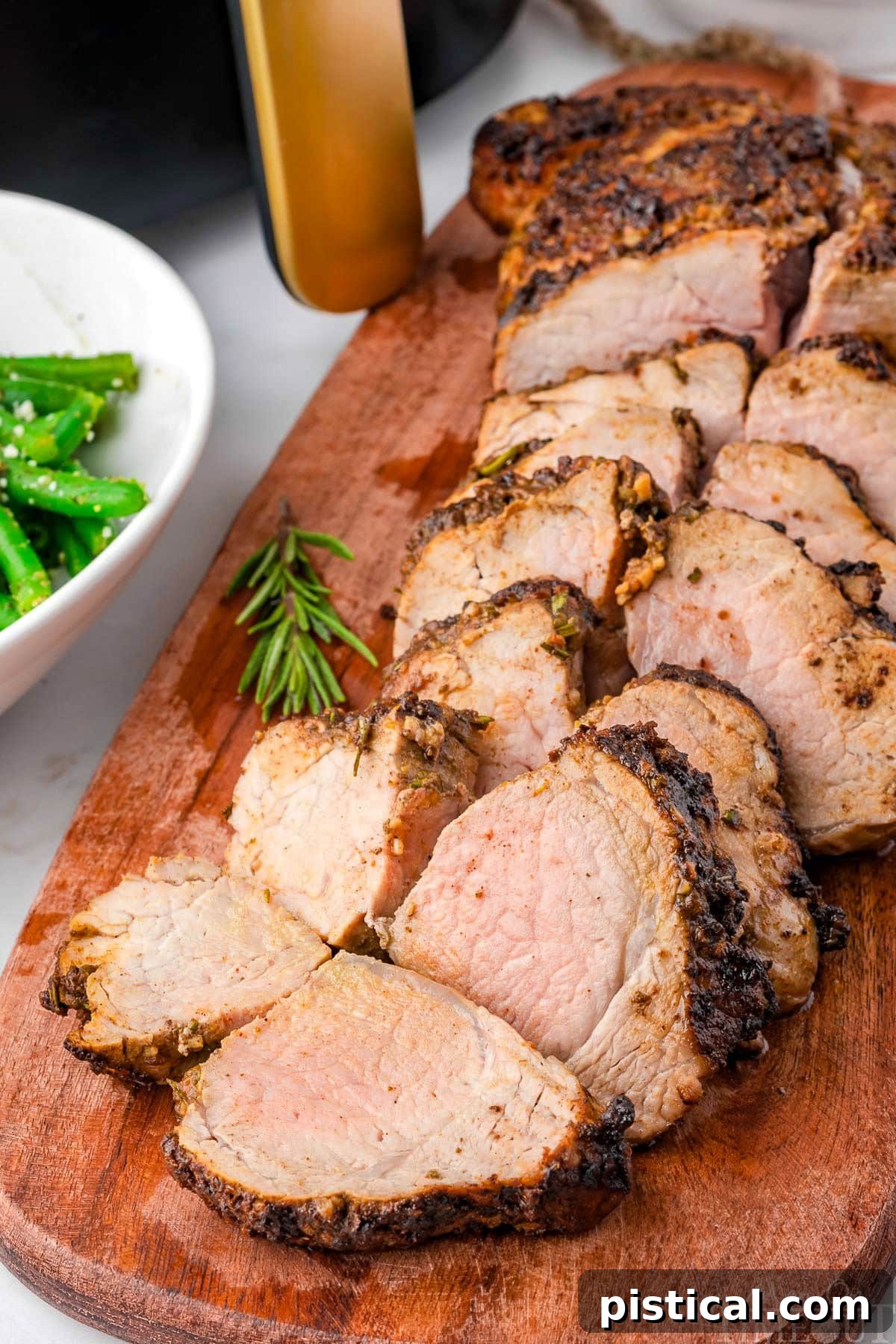 Air fryer pork tenderloin cut into pieces on a wood cutting board with air fryer in background.
