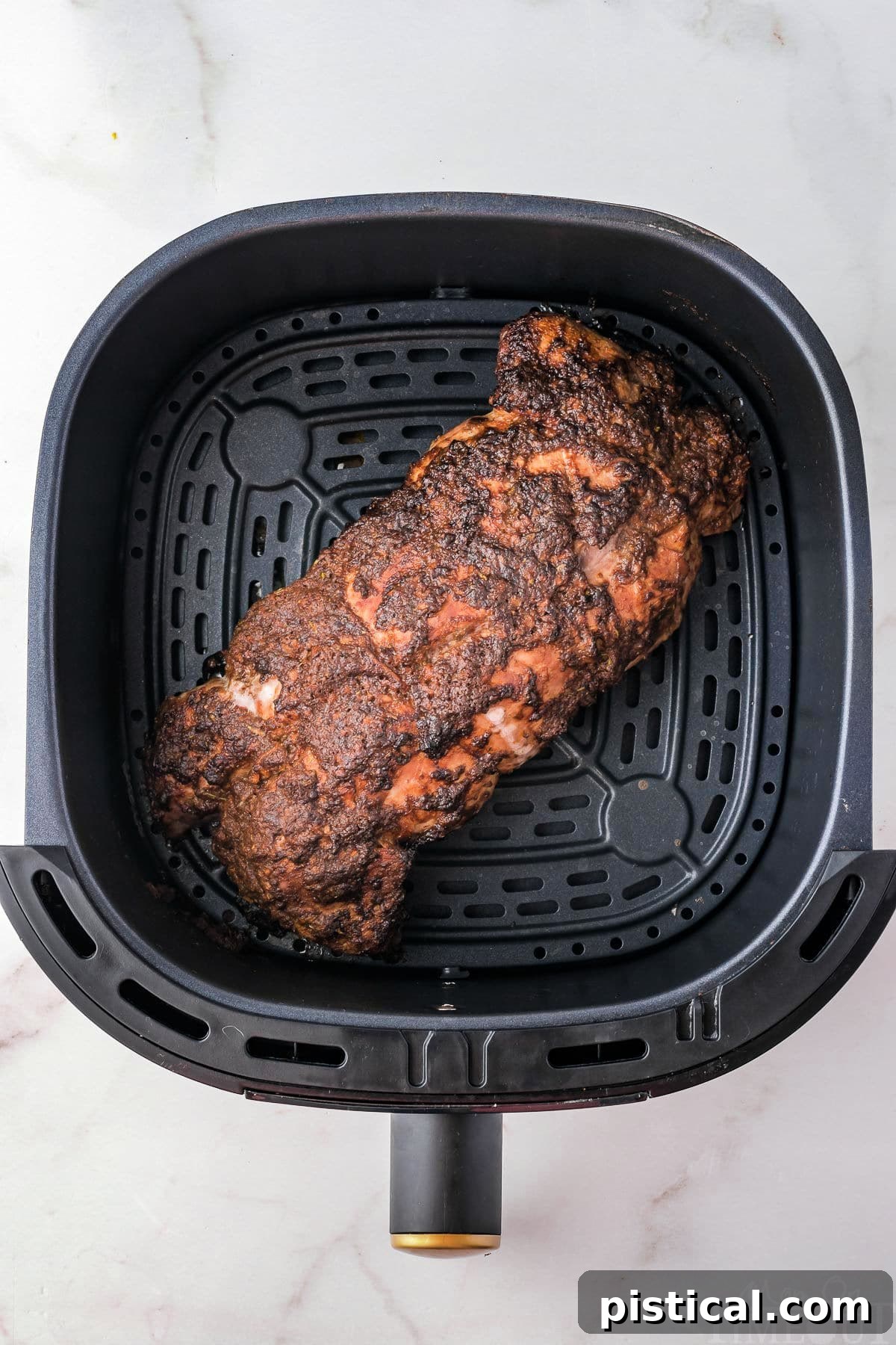 Top down view of pork tenderloin in air fryer sitting on white surface.