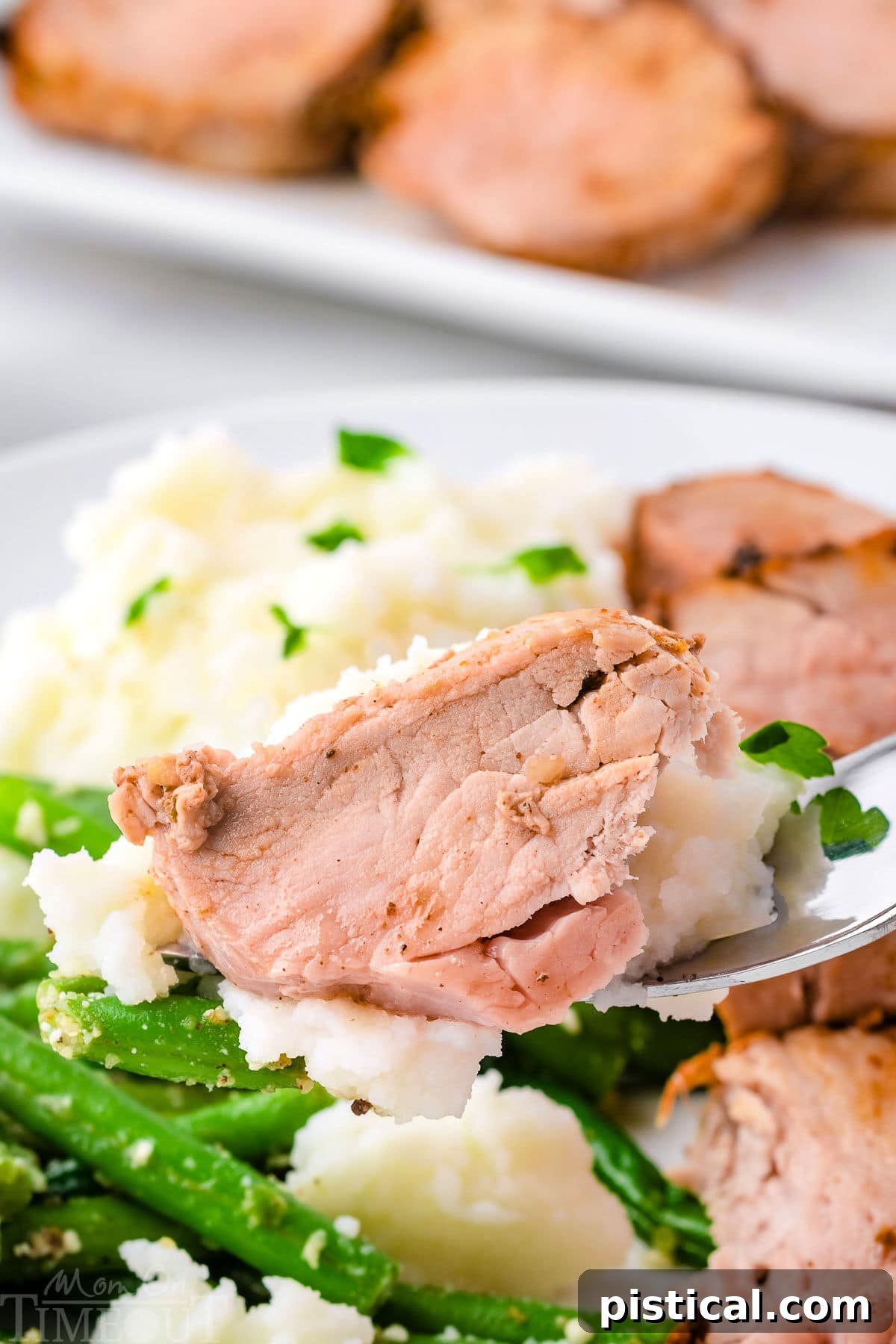 Forkful of pork tenderloin being lifted up from a plate with mashed potatoes and green beans.
