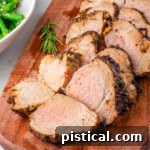 Air fryer pork tenderloin cut into pieces on a wood cutting board with air fryer in background.
