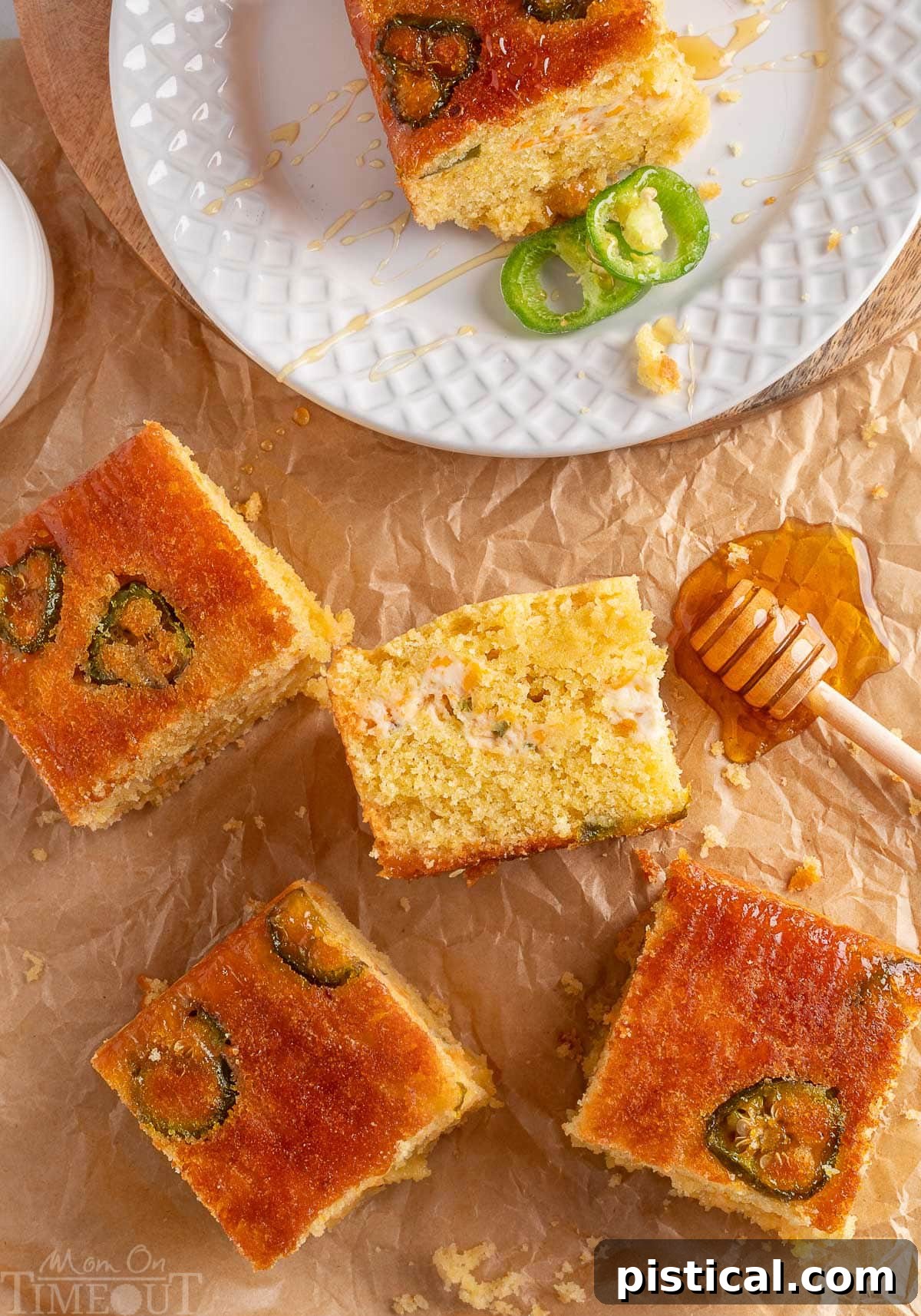 Jalapeno cornbread cut into squares on brown parchment paper. One piece is on a white plate with two slices of jalapeno next to it.