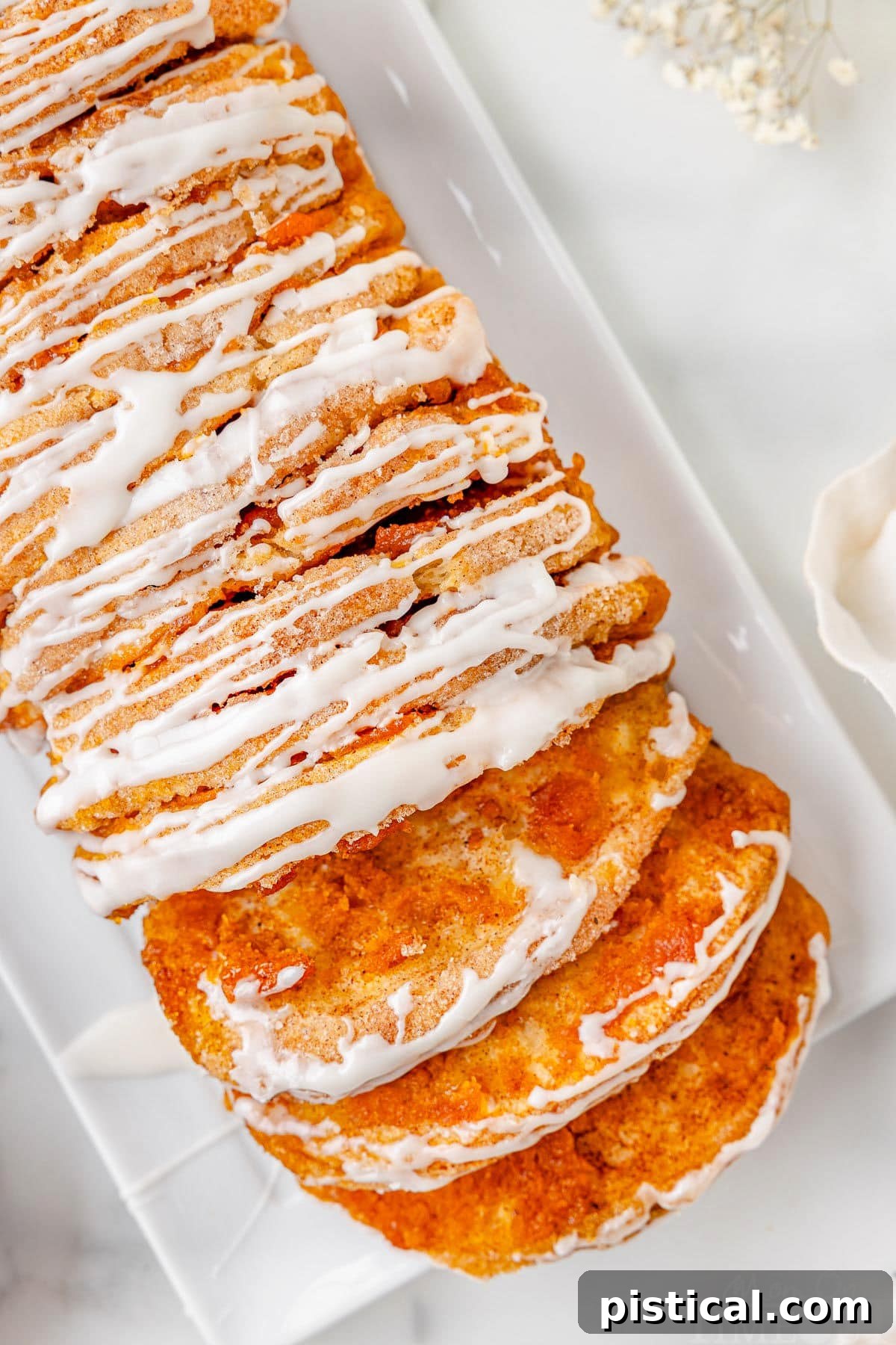 Top down view of pumpkin pull apart bread recipe topped with a simple vanilla glaze on a white rectangular plate. Two slice have been pulled away from the loaf.