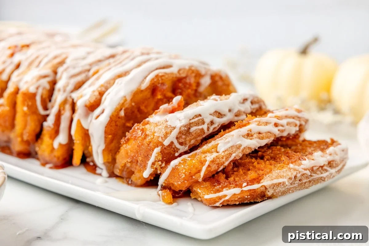 Side profile shot of pull apart pumpkin bread on a white plate topped with a glaze. Pieces have been pulled down to show the pumpkin filling.