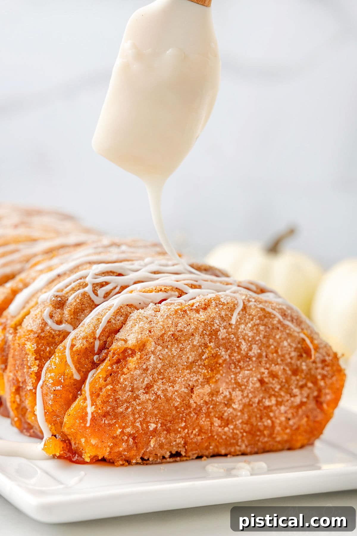 Icing being drizzle on top of a pumpkin pull apart bread made with refrigerated biscuits.