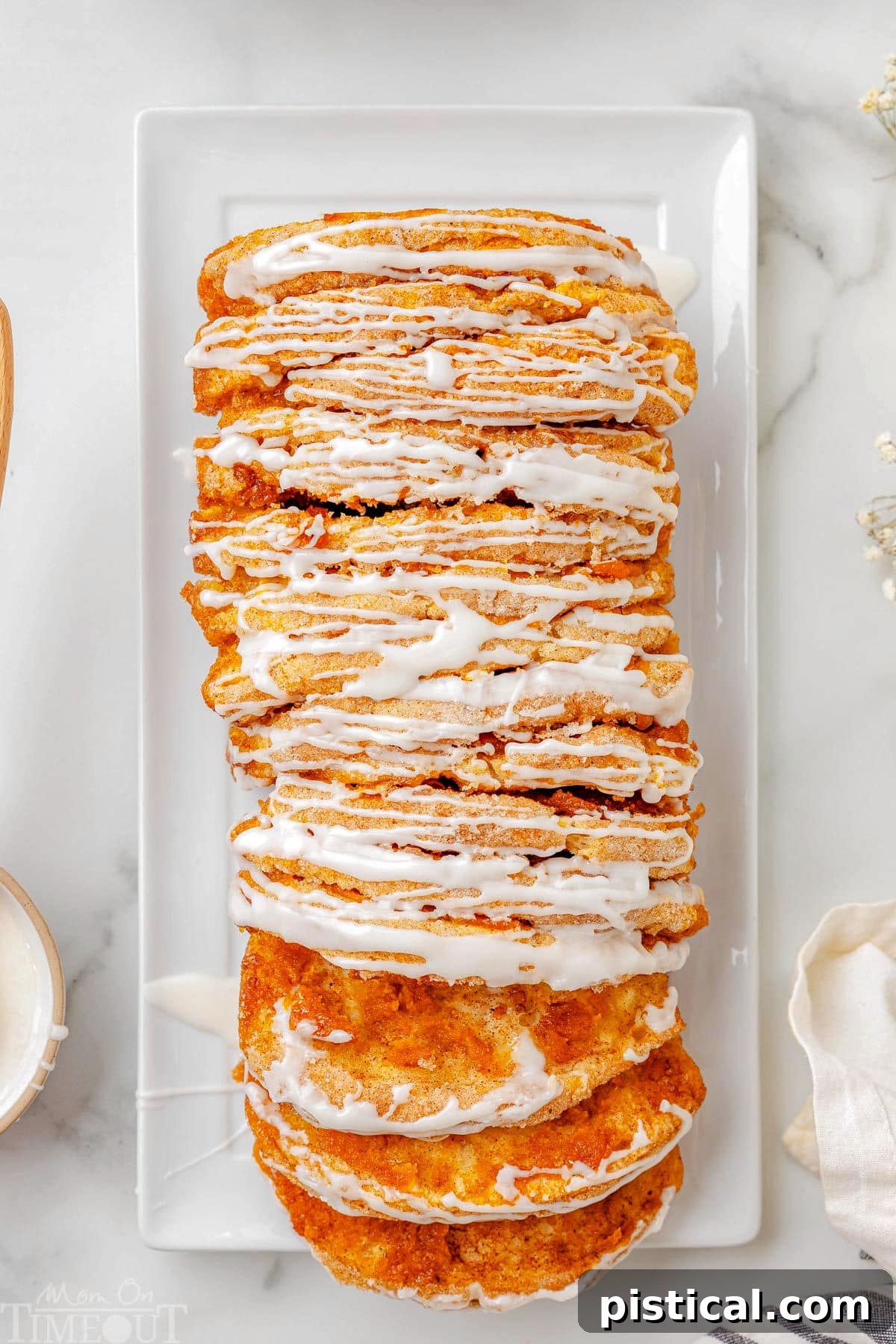 Top down view of pumpkin pull apart bread recipe topped with a simple vanilla glaze on a white rectangular plate. Two slice have been pulled away from the loaf.