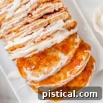 Top down view of pumpkin pull apart bread recipe topped with a simple vanilla glaze on a white rectangular plate. Two slice have been pulled away from the loaf.