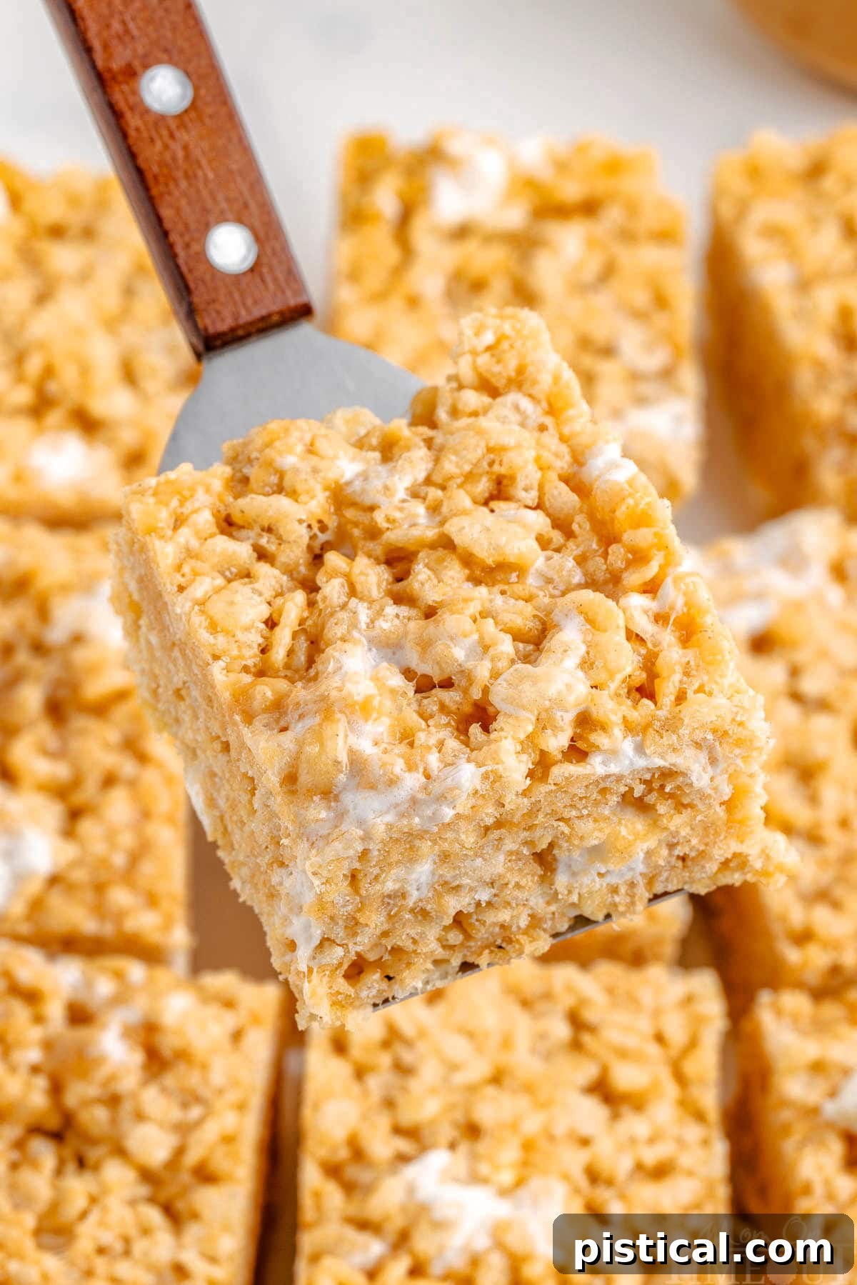 Metal server holding up a peanut butter rice krispie treat over the rest of the cut treats, showing off its perfect square shape.